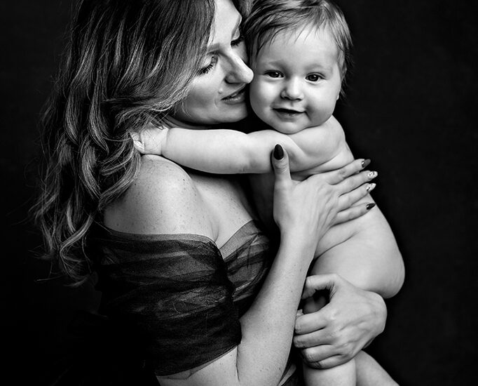 Foto di famiglia in bianco e nero, in cui la madre tiene in braccio il bambino che sorride. Fotografia in bianco e nero di famiglia mamma con bambino Italia