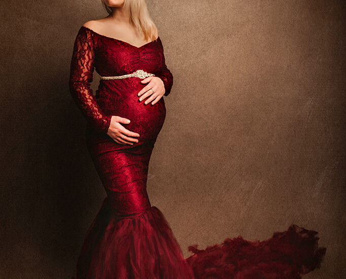 Foto Fine Art a colori di maternità di una donna incinta con un vestito rosso e delle piume sulla testa. Fotografia Fine Art a colori di maternità di una donna incinta con un vestito rosso Italia