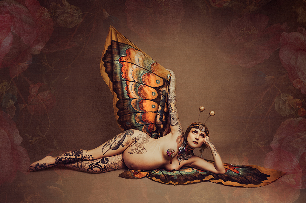 Foto Fine Art a colori di maternità di una donna incinta nuda tatuata con delle ali di farfalla, distesa per terra. Fotografia Fine Art a colori di maternità di una donna nuda tatuata con delle ali di farfalla, distesa per terra Italia
