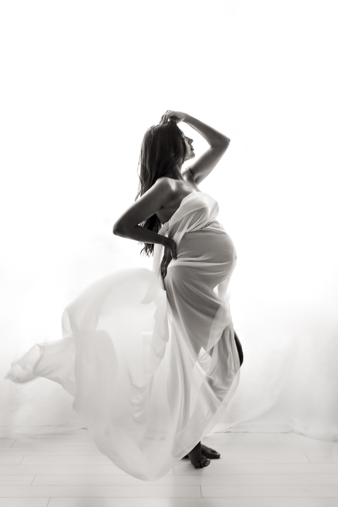 Foto Fine Art in bianco e nero di maternità in studio, di una donna incinta coperta da un velo bianco. Fotografia in bianco e nero di maternità in studio con donna con velo bianco Trieste