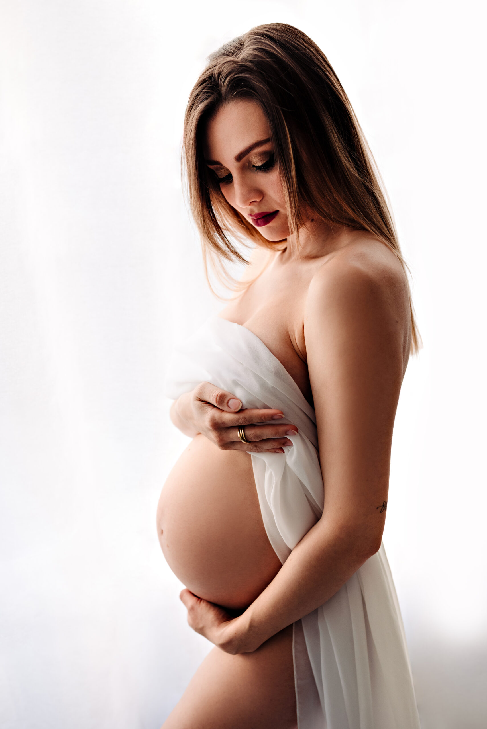 Foto artistica a colori di maternità di una donna incinta, coperta da un telo bianco. Fotografia artistica di maternità di una donna incinta a colori, con velo bianco Trieste