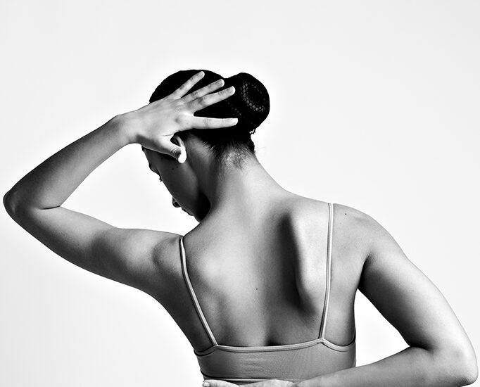 Foto in bianco e nero di una ragazza su sfondo bianco con le braccia dietro la schiena. Fotografia ritratto in bianco e nero ragazza in body Italia