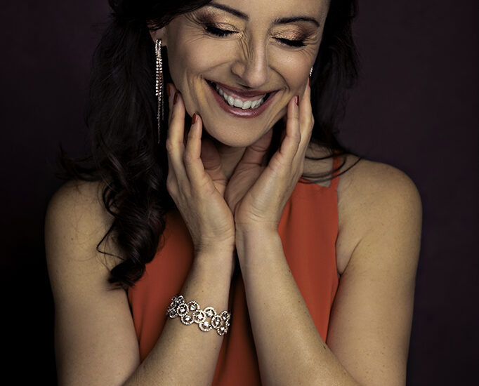 Foto ritratto artistico a colori di una donna con un vestito rosso e dei gioielli argentati, mentre ride. Fotografia ritrattistica di una donna che sorride a colori in studio Italia