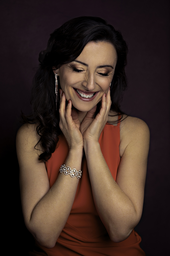 Foto ritratto artistico a colori di una donna con un vestito rosso e dei gioielli argentati, mentre ride. Fotografia ritrattistica di una donna che sorride a colori in studio Italia