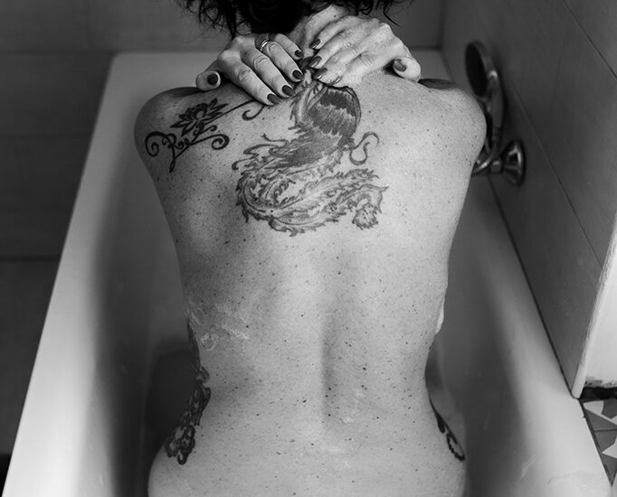 Foto in bianco e nero di una donna nuda in una vasca, con un tatuaggio sulla schiena. Fotografia sensuale donna boudoir Trieste