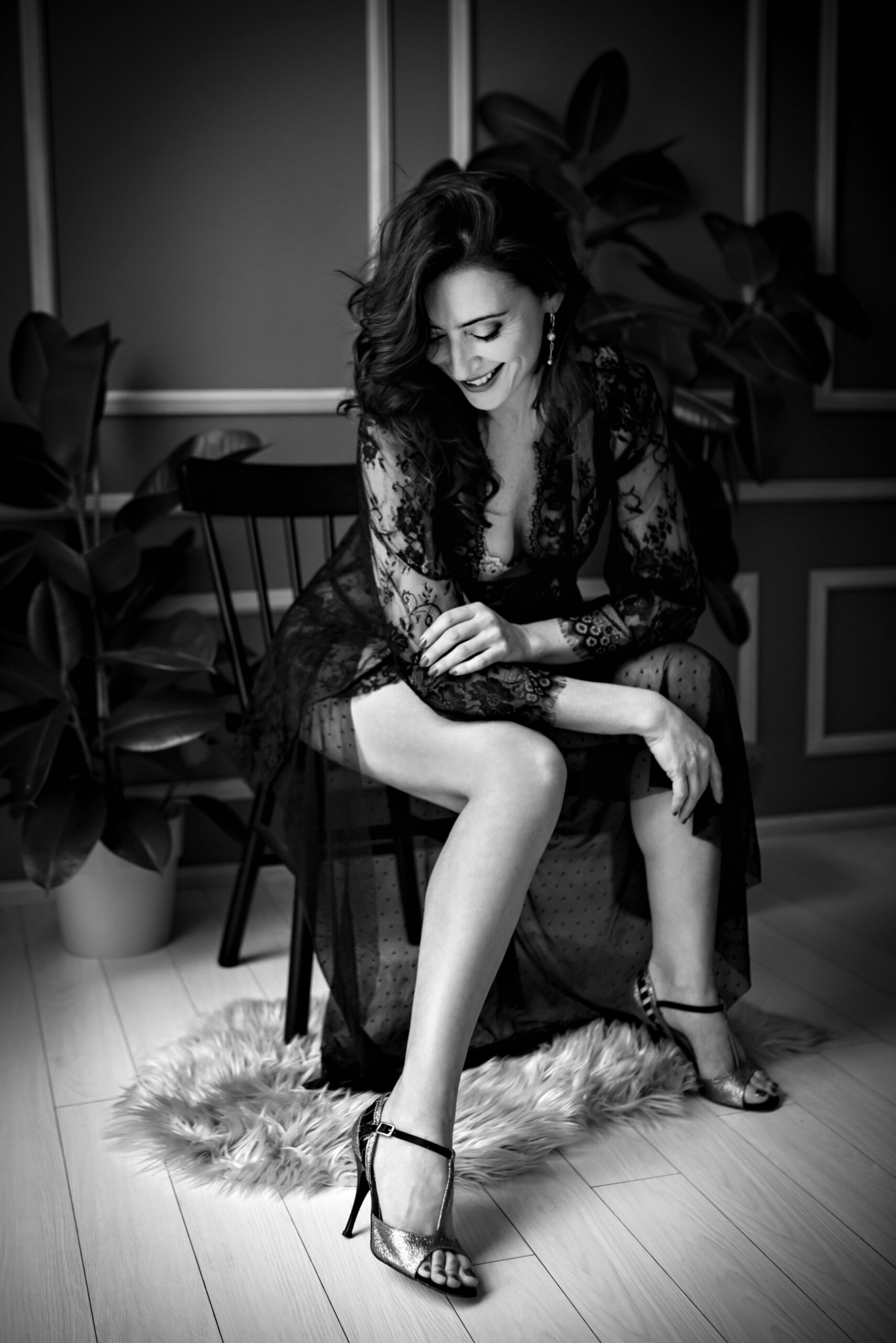 Foto in bianco e nero di una donna in initmo con sopra un vestito nero trasparente scollato, mentre sorride. Fotografia in bianco e nero boudoir donna Trieste