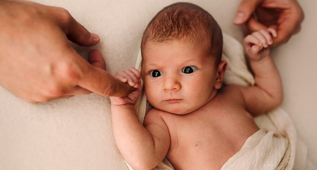 Foto a colori di un neonato avvolto da delle stoffe bianche. Fotografia a colori di un neonato Trieste
