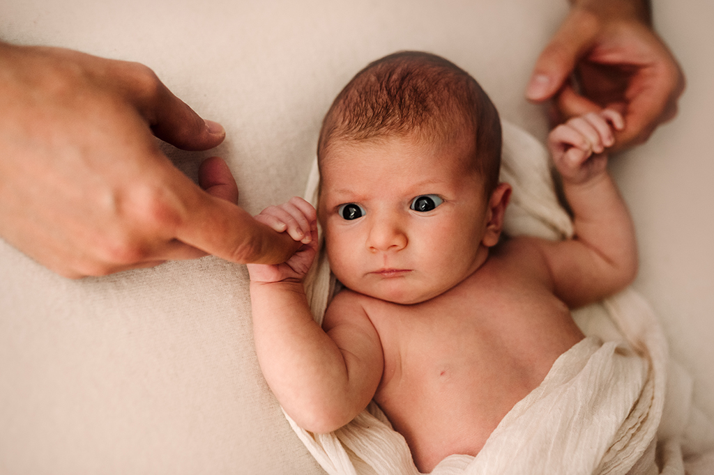 Foto a colori di un neonato avvolto da delle stoffe bianche. Fotografia a colori di un neonato Trieste