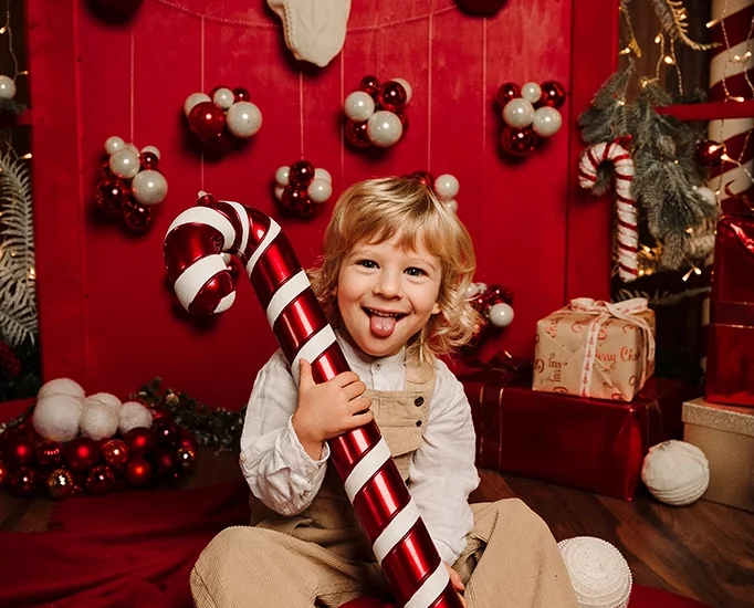Foto ritrattistica a colori a tema natalizio di una bambino con in mano un bastocino di zucchero. Fotografia ritrattistica a tema Natale a colori bimbo Trieste