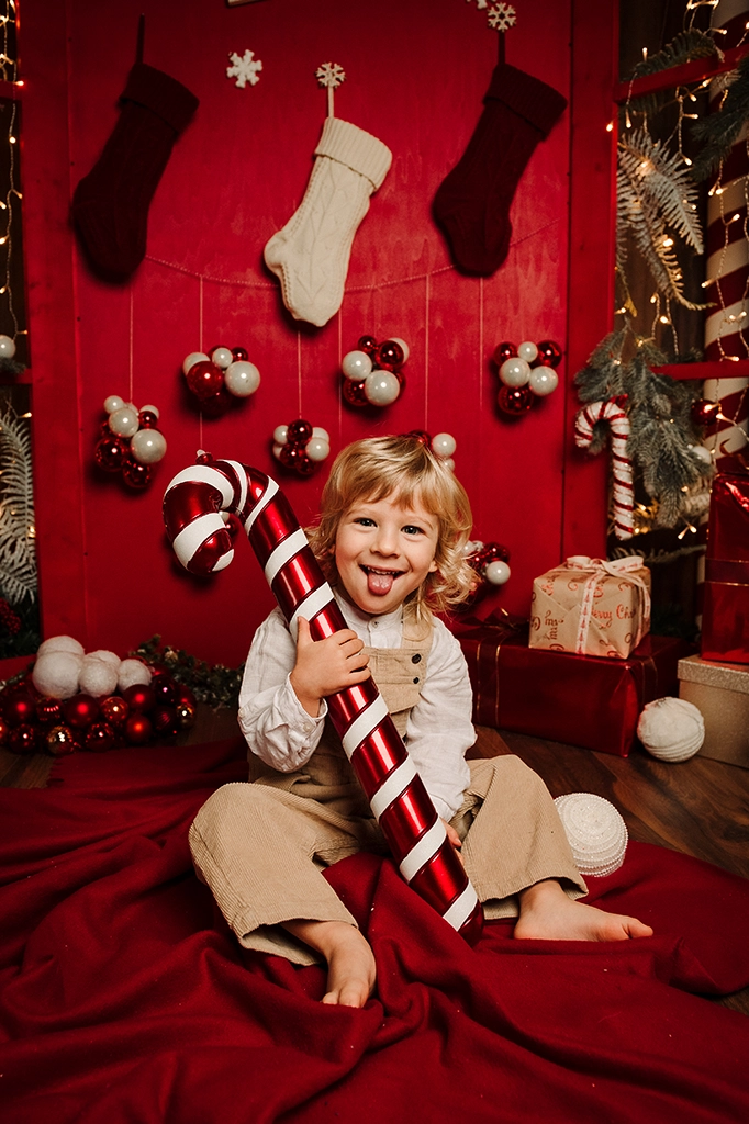 Foto ritrattistica a colori a tema natalizio di una bambino con in mano un bastocino di zucchero. Fotografia ritrattistica a tema Natale a colori bimbo Trieste