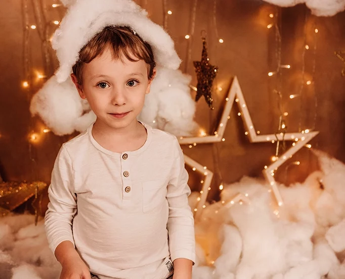 Foto a tema natalizio di un bambino tra le nuvole e le stelle dorate, messo in ginocchioni con una nuvola in testa. Fotografia di un bambino a tema natalizio tra le nuvole Trieste