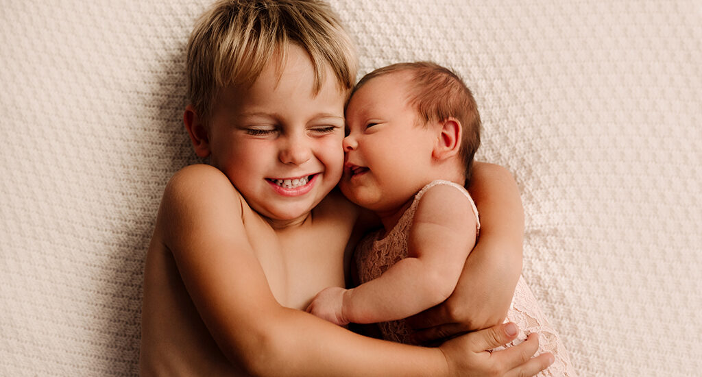 Foto di famiglia a colori, in cui il fratello abbraccia il neonato. Fotografia a colori di famiglia fratello con neonato Italia