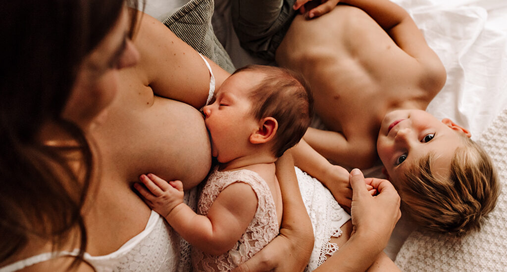 Foto di famiglia a colori, in cui la mamma allatta il neonato e l'altro il bambino sta vicino. Fotografia in bianco e nero di famiglia con neonato e fratello Italia