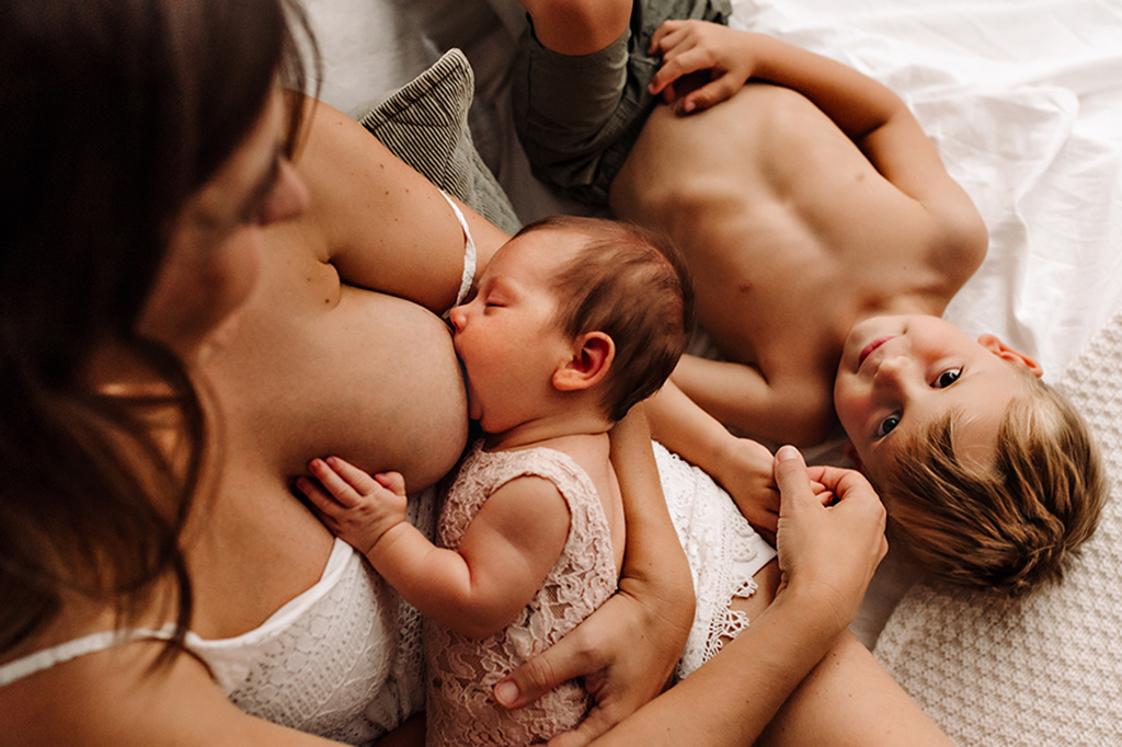 Foto di famiglia a colori, in cui la mamma allatta il neonato e l'altro il bambino sta vicino. Fotografia in bianco e nero di famiglia con neonato e fratello Italia