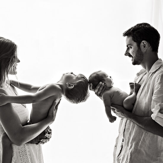 Foto di famiglia in bianco e nero, in cui i genitori tengono in braccio uno il neonato e l'altro il bambino. Fotografia in bianco e nero di famiglia con neonato Italia