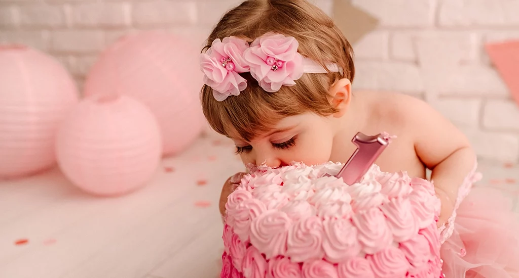 Foto a colori di una bimba sporca di torta mentre mangia con dei fiorellini rosa sulla testa. Fotografia a colori di una bimba sporca di torta mentre mangia Trieste