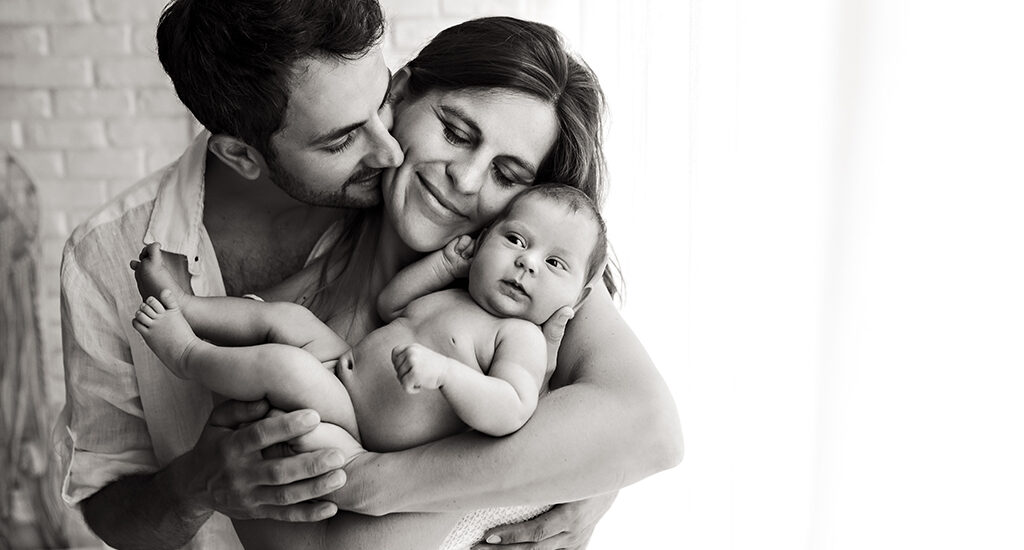 Foto di famiglia in bianco e nero, in cui i genitori tengono in braccio e si abbracciano. Fotografia in bianco e nero di famiglia con neonato nudo Italia