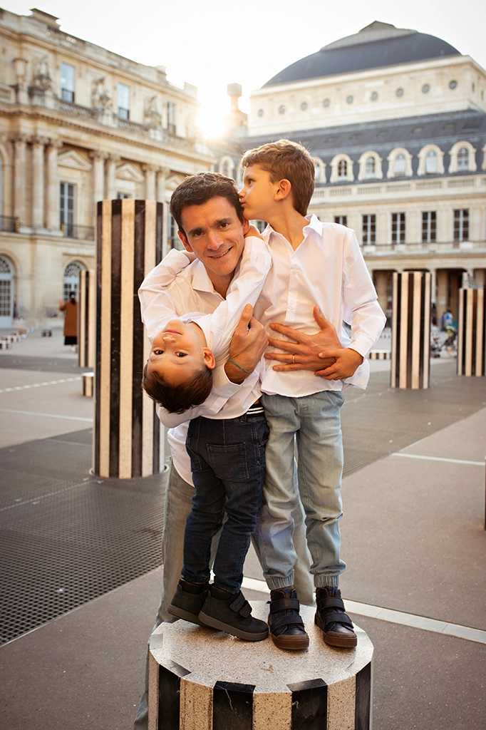 Foto a colori fuori studio a Parigi, di un papà con i figli che si abbracciano. Fotografia a colori di una famiglia a Parigi Italia