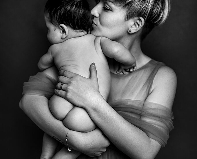 Foto in bianco e nero in studio di famiglia, di una mamma con il figlio nudo in braccio. Fotografia in bianco e nero di famiglia mamma e figlio Italia