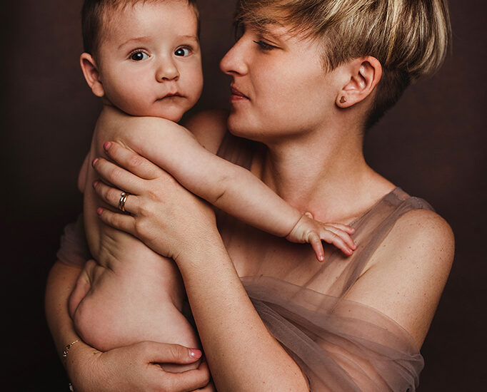Foto a colori in studio di famiglia, di una mamma con il figlio nudo in braccio. Fotografia a colori di famiglia mamma e figlio Italia