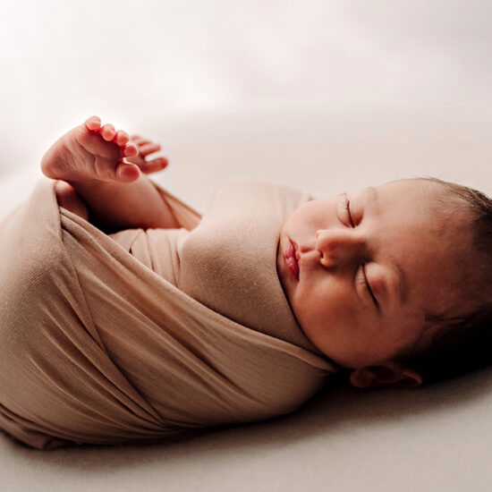 Foto a colori di un neonato che dorme avvolto da delle stoffe beige. Fotografia a colori di un neonato che dorme Trieste