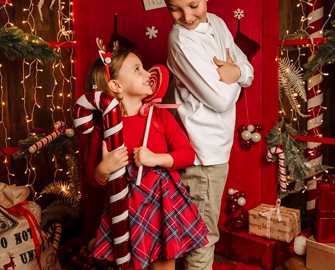 Foto ritrattistica a colori a tema natalizio con due bambini, fratello e sorella con in mano un bastoncino di zucchero e un lecca lecca. Fotografia ritrattistica a colori a tema Natale con bimbi Trieste
