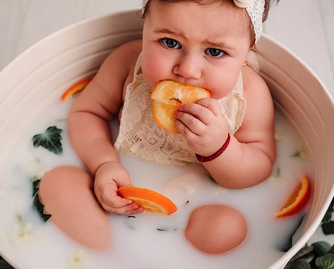 Foto a colori di una bimba mentre mangia arance in un secchio di latte con della frutta. Fotografia a colori di una bimba in un secchio di latte che mangia della frutta Italia