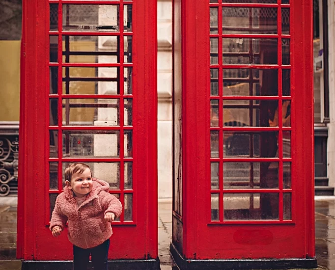 Foto a colori fuori studio di una bambina davanti a delle cambine telefonoiche a Londra. Fotografia a colori di una bambina con cabine telefoniche a Londra Italia