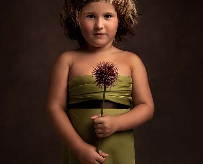 Foto ritrattistica artistica a colori con una bambina che tiene un fiore viola in mano ed un vestito verde. Fotografia artistica ritrattistica a colori Italia
