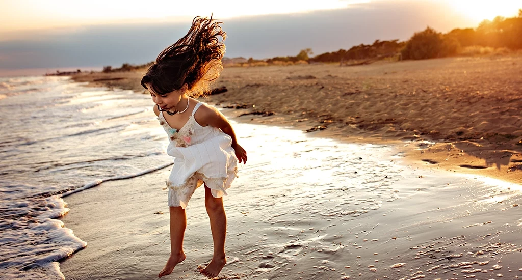 Foto fuori studio a colori di una bambina sulla riva della spiaggia che salta. Fotografia fuori studio a colori Italia
