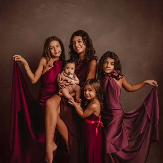Foto a colori artistica di famiglia con cinque bambine di età differenti, tutte con un vestito in colore bordeaux. Fotografia artistica a colori di famiglia Italia