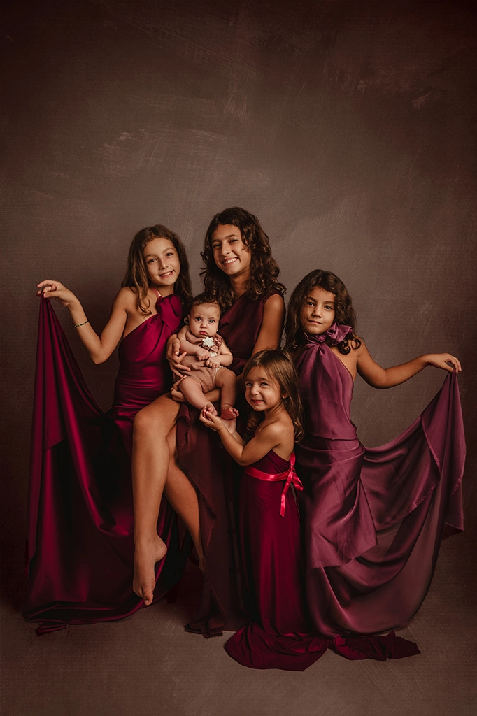 Foto a colori artistica di famiglia con cinque bambine di età differenti, tutte con un vestito in colore bordeaux. Fotografia artistica a colori di famiglia Italia