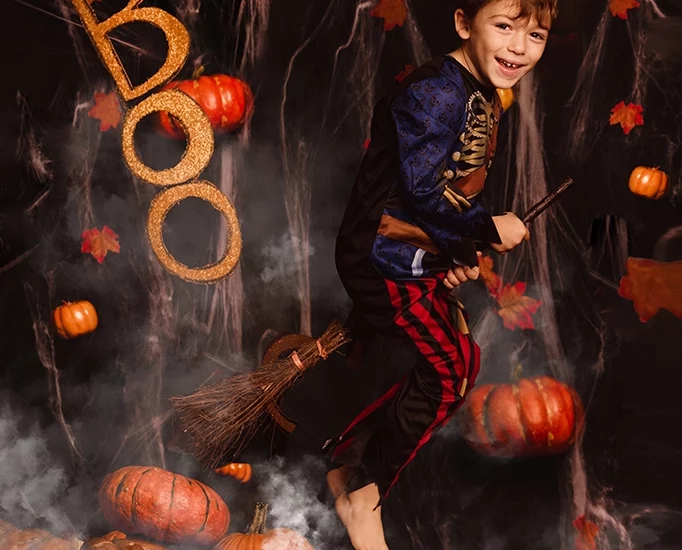 Foto ritrattistica a colori a tema Halloween di un bambino vestito da pirata, con sotto delle zucche e che ola con sotto una scopa. Fotografia ritrattistica a tema Halloween a colori bambino Italia