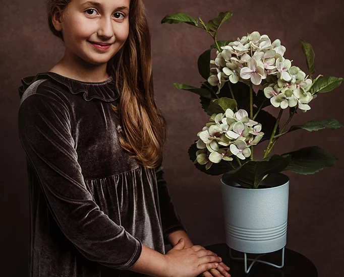 Foto ritratto a colori di una bambina vicino ad un vaso di fiori. Fotografia a colori Italia