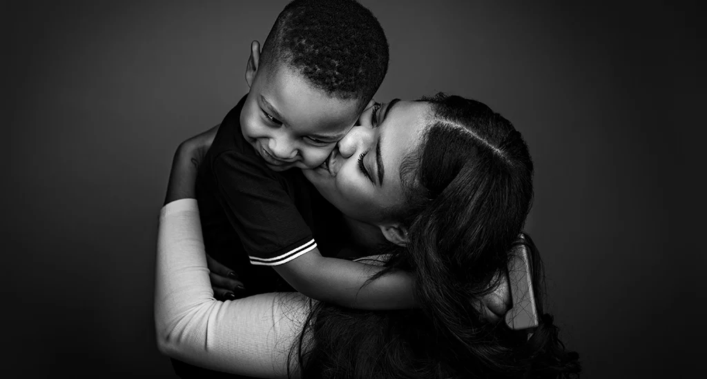 Foto ritratto in bianco e nero di una mamma con il figlio mentre lo tiene in braccio. Fotografia ritrattistica in bianco e nero Italia
