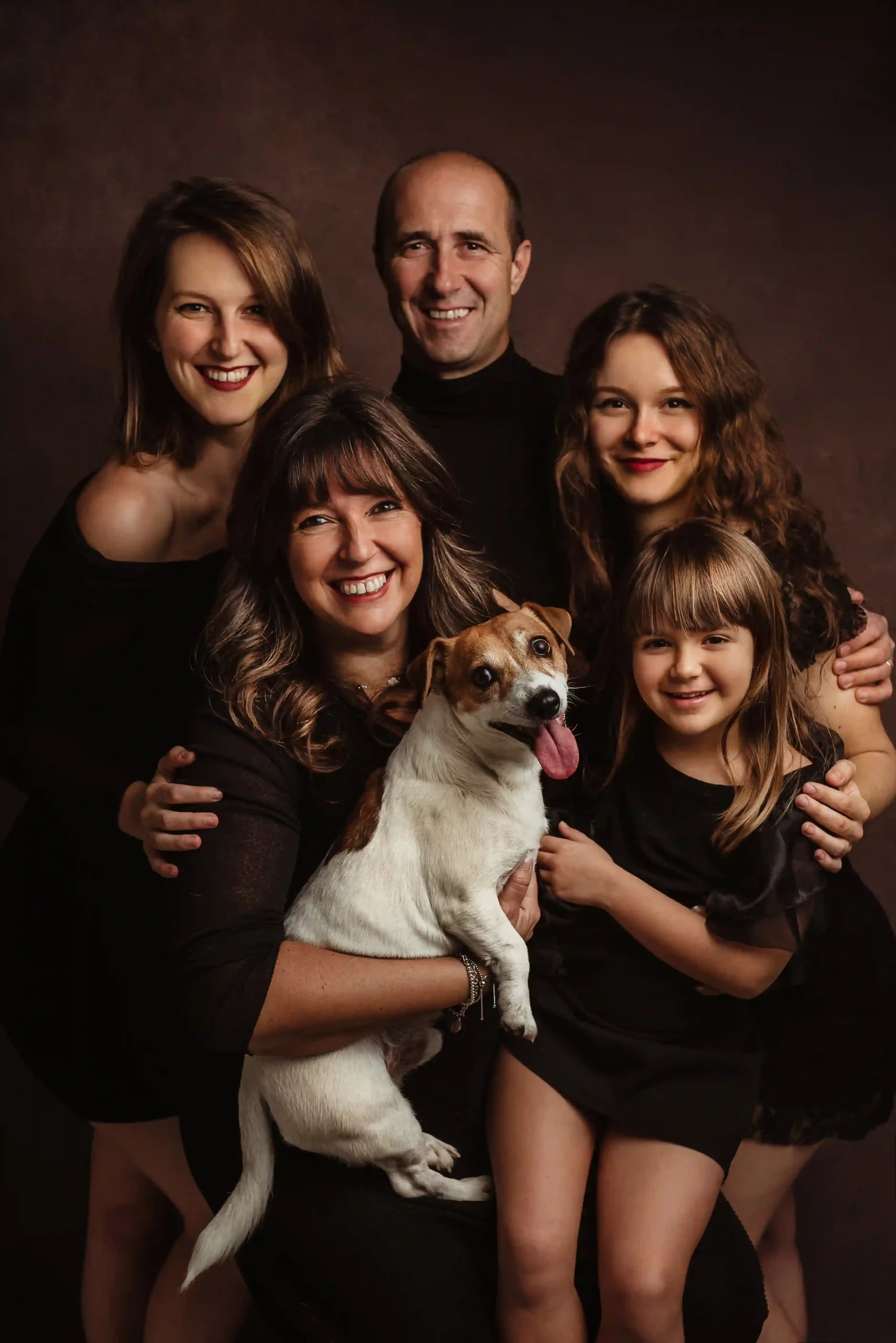 Foto ritrattistica di famiglia a colori con cane su sfondo scuro, tutti vestiti di nero. Fotografia di famiglia Italia