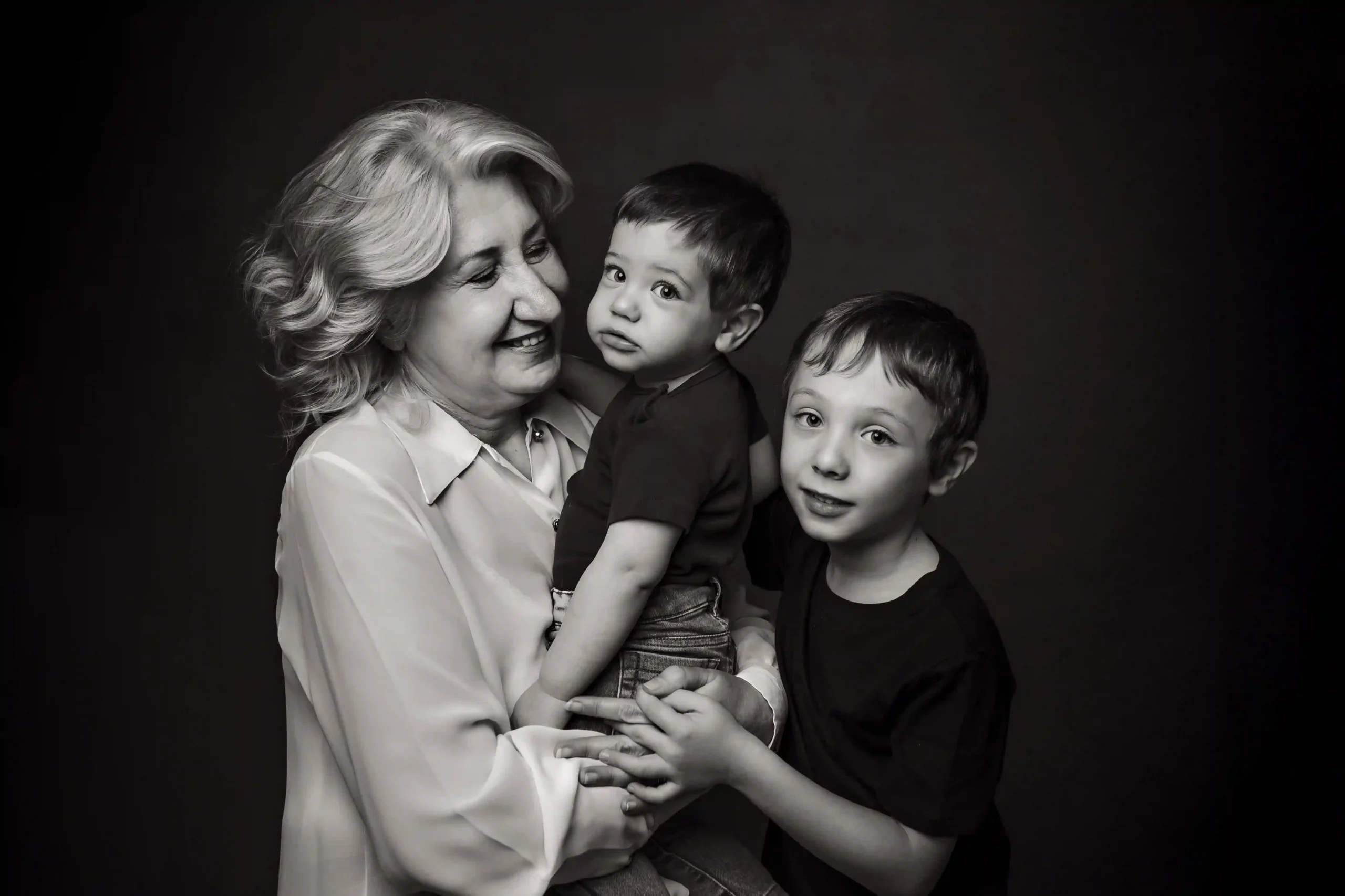 Foto in bianco e nero di famiglia con bambini vetsiti di nero e la nonna con la camicia bianca che tiene in braccio il bambino piccolo. Fotografia ritratto in bianco e nero Trieste