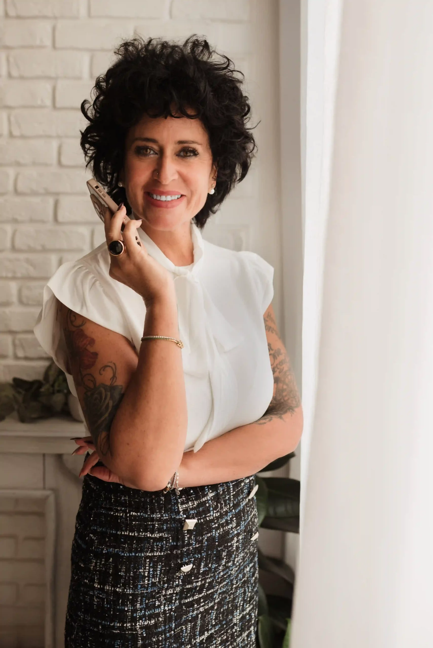 Foto ritratto donna business tatuata a colori mentre parla al telefono con di fianco una tenda bianca. Fotografia ritrattistica donna Trieste