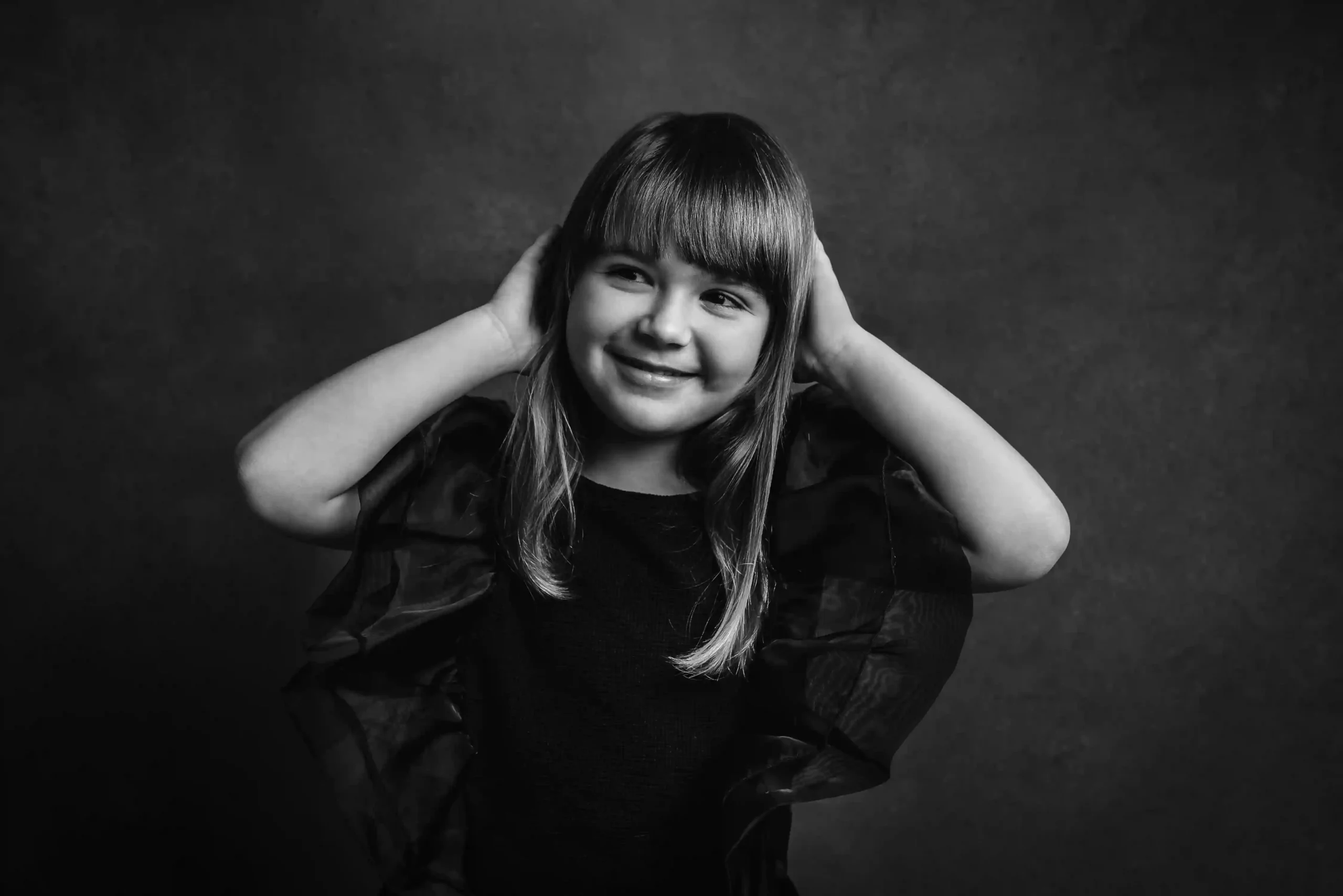 Foto di una bambina in bianco e nero che sorride con le mani poggiate sulla testa. Fotografia in bianco e nero Trieste