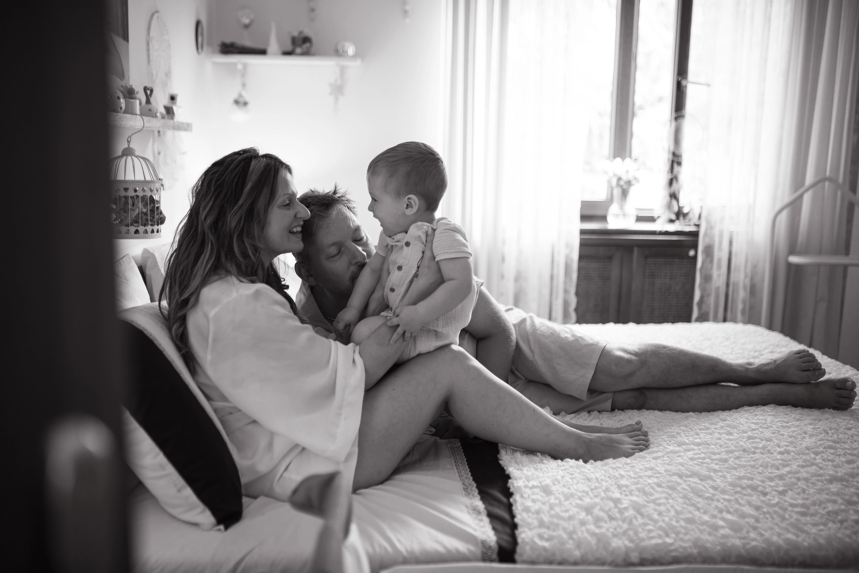 Reportage di famiglia in bianco e nero, in casa di due genitori a letto con il bambino, mentre si guardano. Reportage di famiglia in bianco e nero Trieste