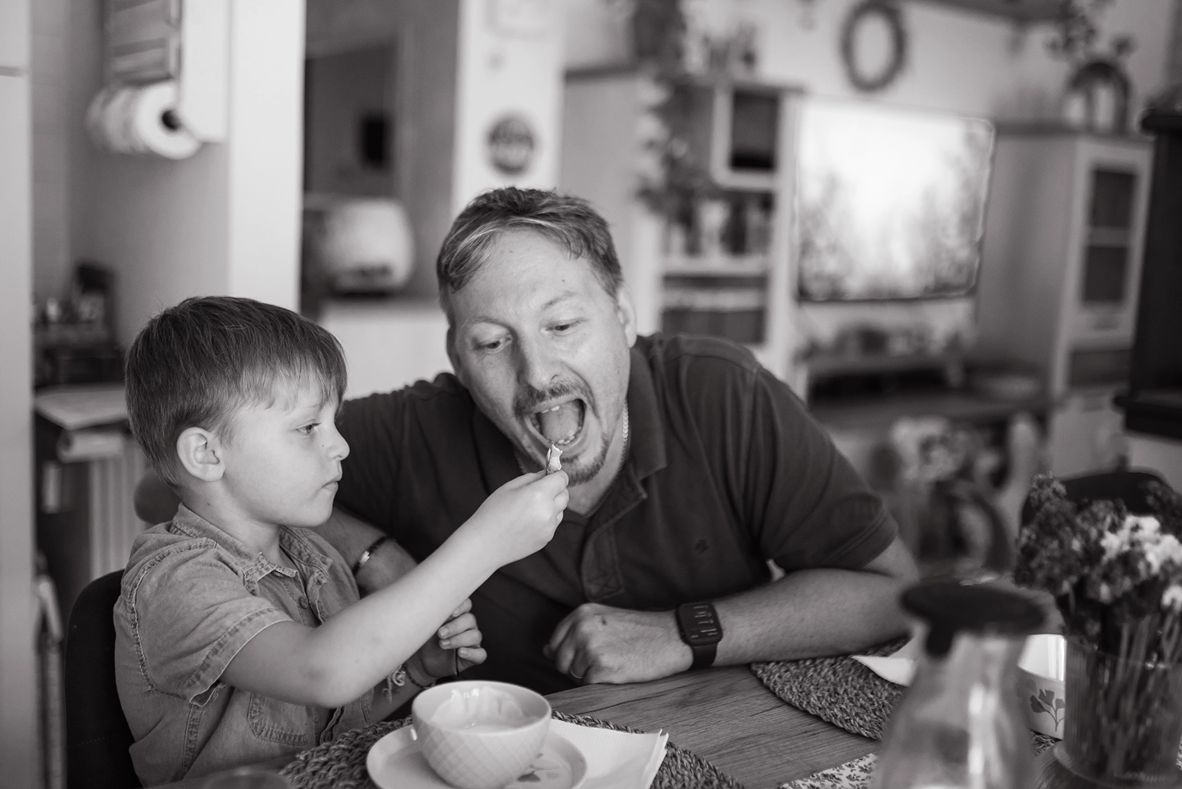 Reportage di famiglia in bianco e nero in casa di un papà con il figlio a tavola, mentre fanno colazione. Reportage di famiglia in bianco e nero papà e figlio Trieste
