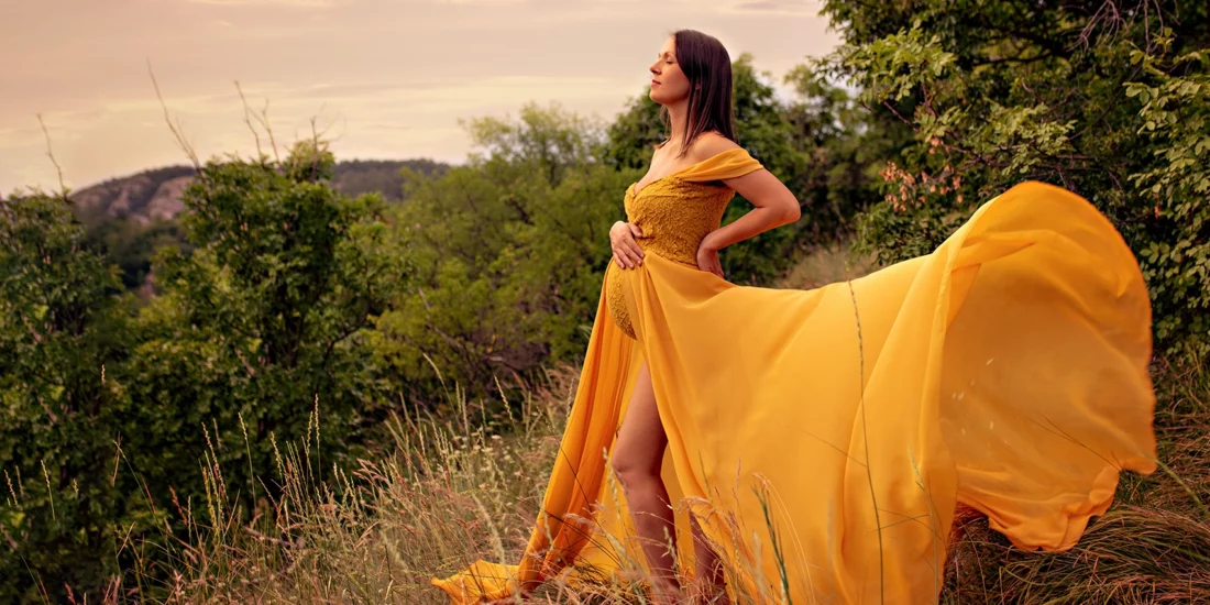 Foto fuori studio a colori di una donna incinta con un vestito lungo giallo, tra l'erba. Fotografia fuori studio a colori di maternità tra l'erba Trieste