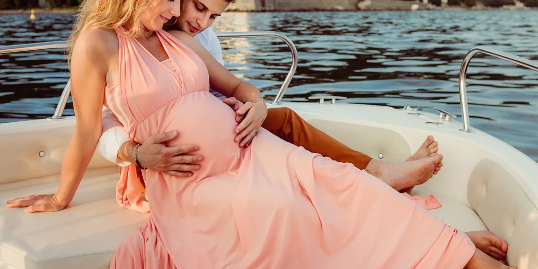 Foto fuori studio a colori di una coppia con una donna incinta con un vestito lungo rosa, su una barca nel mare. Fotografia fuori studio a colori di maternità su una barca nel mare Trieste